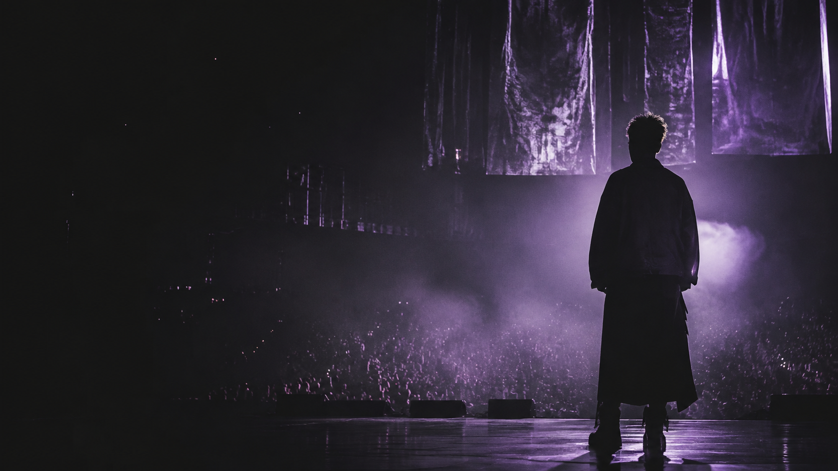 An artist facing an audience from a dark stage washed in lavender light
